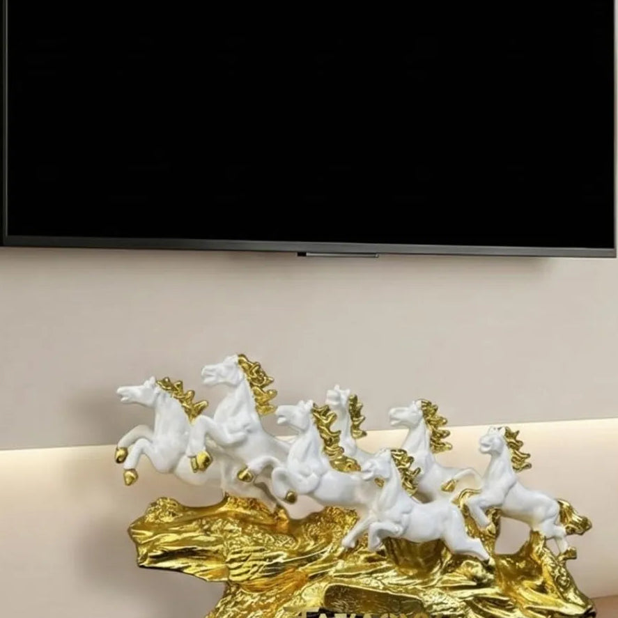Decorative sculpture of horses on a gold base on a shelf with a TV in the background.